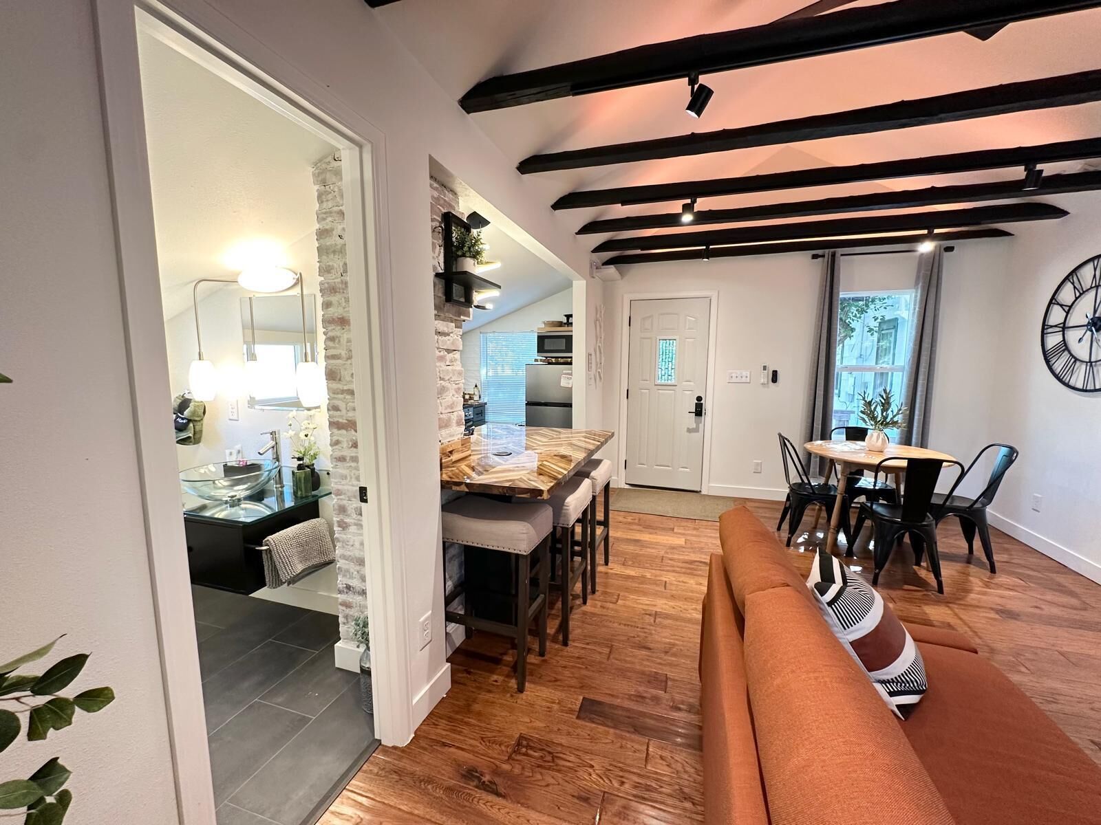 A modern interior with a wooden floor, a dining area with a table and chairs, a bench, and a kitchen visible through an open doorway.