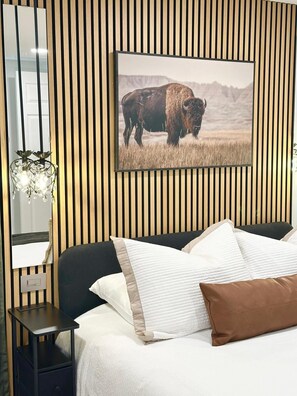 A bedroom with a bed, a nightstand, a wall-mounted mirror, and a picture of a bison. - The Bison Cottage bungalow, a private boutique retreat in Cheyenne. (Cheyenne)