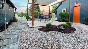 A covered patio area with a table and chairs, surrounded by a gravel pathway and a wooden deck. - The Bison Cottage bungalow, a private boutique retreat in Cheyenne. (Cheyenne)