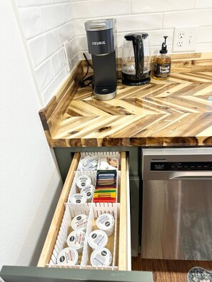 Une cuisine équipée d’une machine à café, d’une bouteille de sirop à la saveur de vanille française et d’un tiroir contenant des capsules de café.