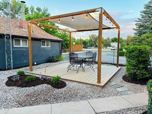 A wooden pergola with string lights, a table with chairs, and a small garden area with pebbles and plants. - The Bison Cottage bungalow, a private boutique retreat in Cheyenne. (Cheyenne)
