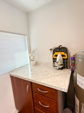 A small kitchen area with a marble countertop, a white vase with flowers, a yellow and black appliance, and a water heater.
