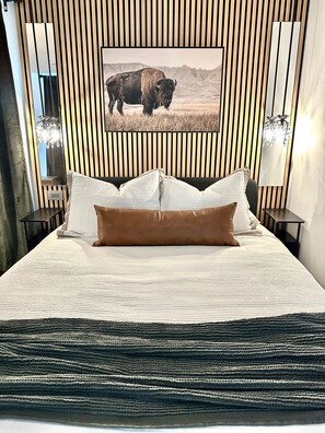 Un lit avec une couvre-lit à motifs, deux oreillers et un tableau représentant un bison accroché au mur.