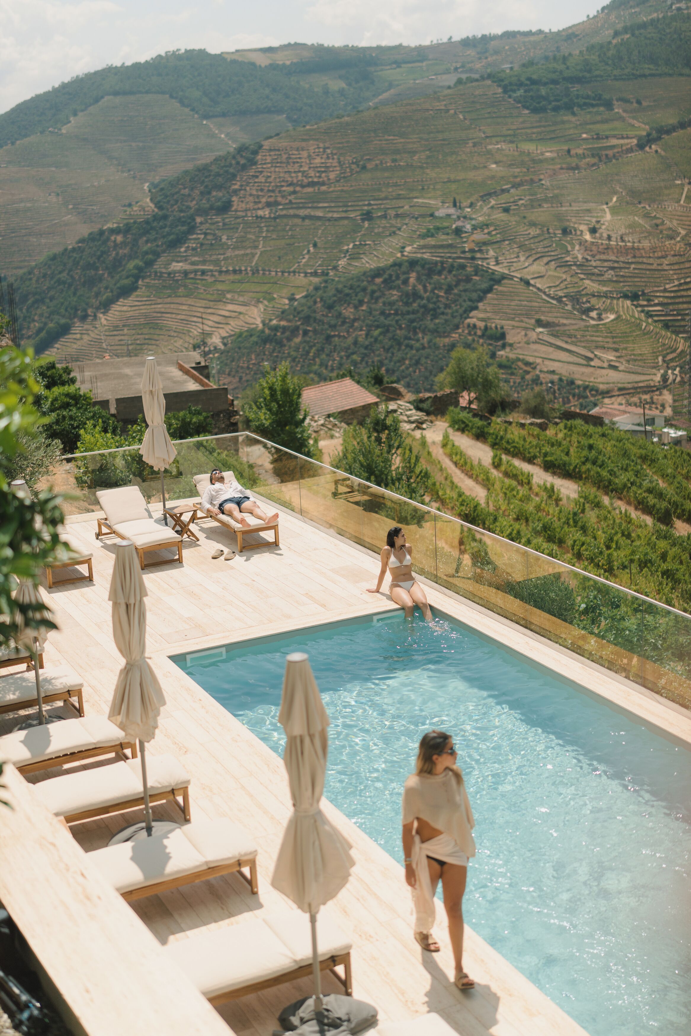 A pool area with lounge chairs and umbrellas, overlooking terraced vineyards.