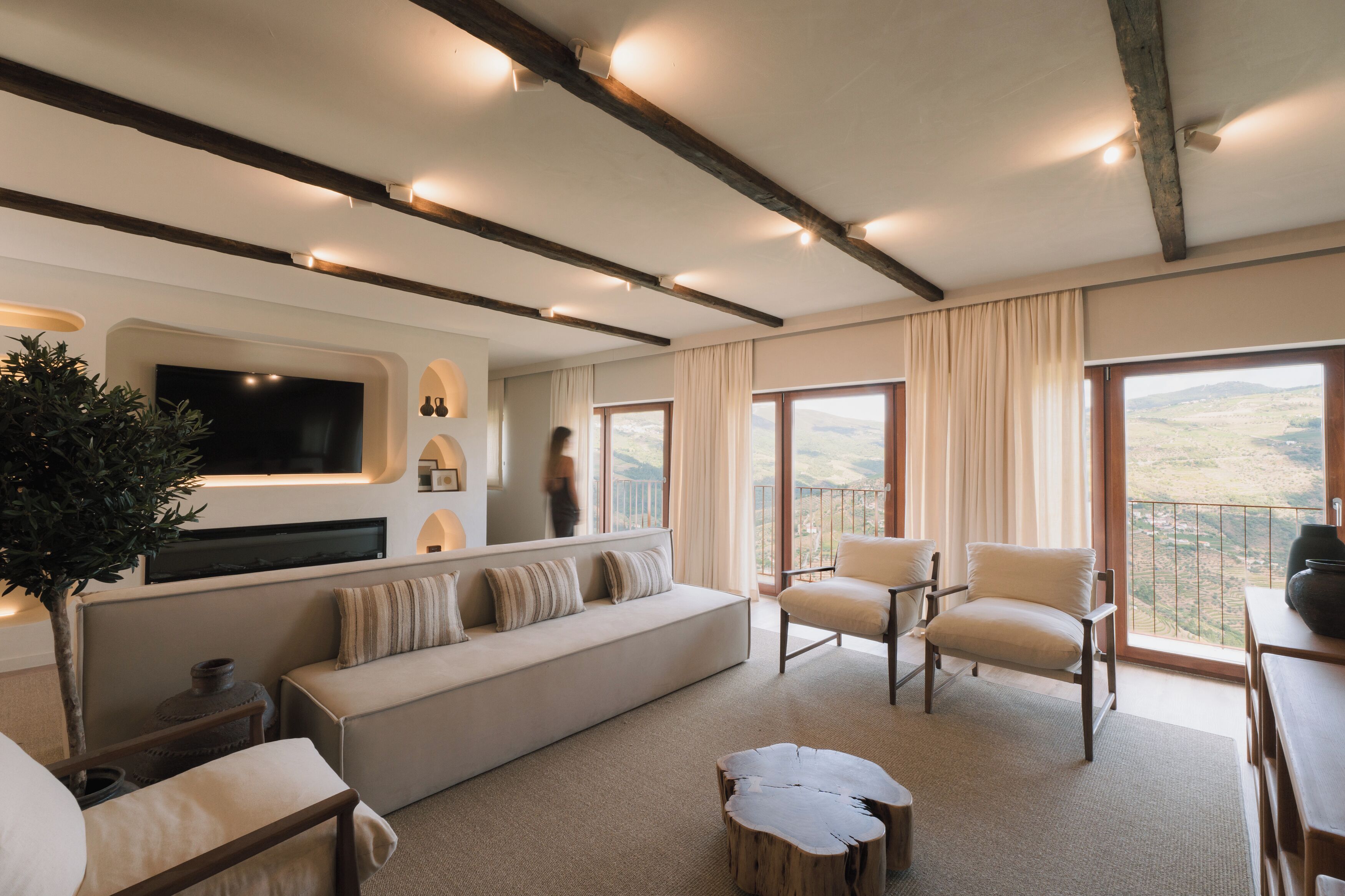Una sala de estar moderna con un sofá, sillones, un televisor de pantalla plana y un ventanal con vistas al campo.