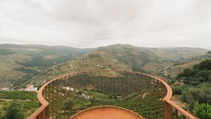 A panoramic view from a balcony with a metal railing, overlooking terraced vineyards and rolling hills. - Douro Olive Hills Village - by FERO (Alijo)