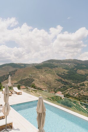 Zona de piscina con sillones de descanso y sombrillas con vistas a viñedos escalonados.