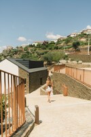 Uma pessoa caminhando por um caminho de pedra, com um muro de pedra de um lado e uma cerca de madeira do outro.