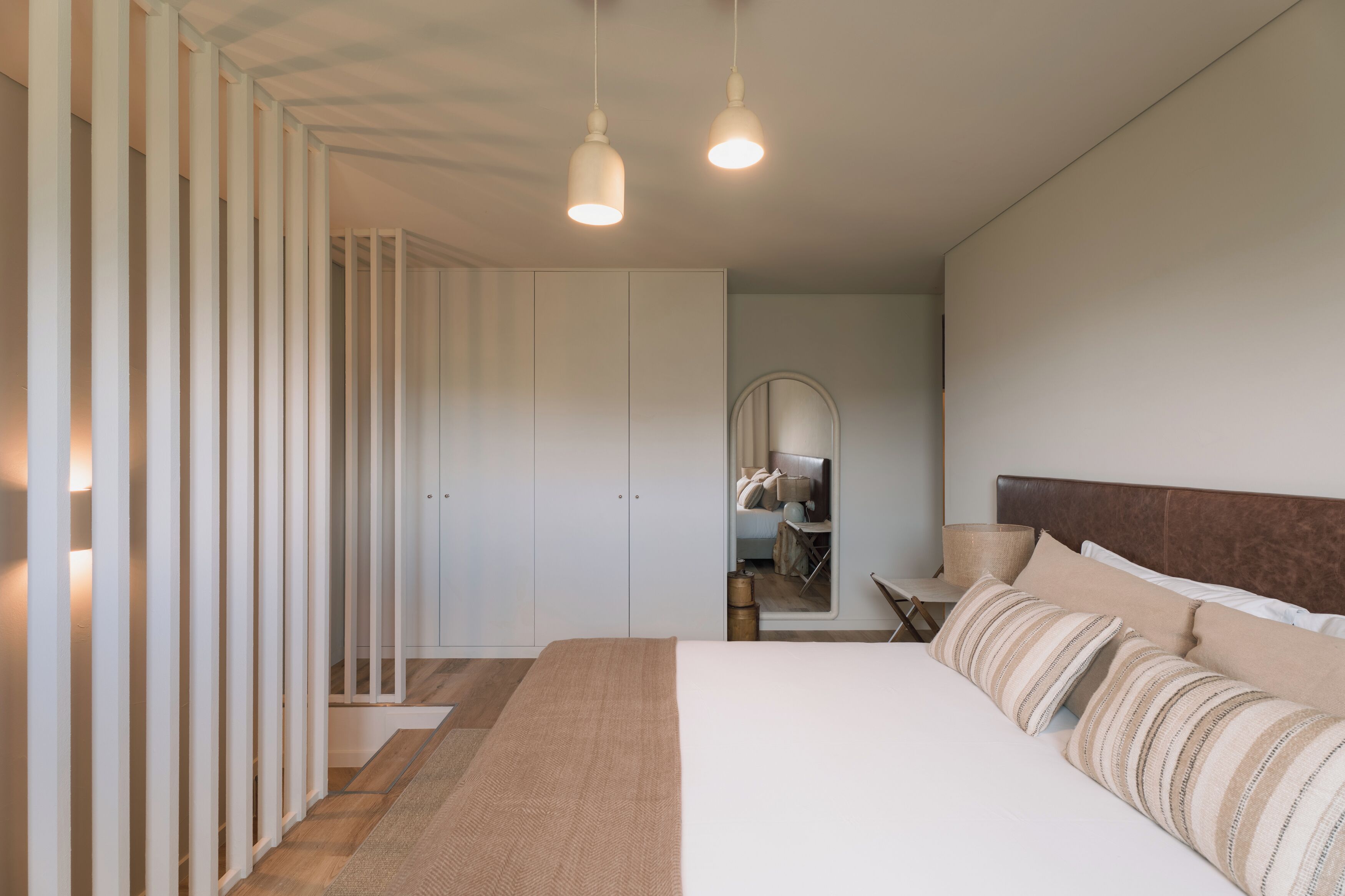 Un dormitorio con una cama grande, suelo de madera, un armario y un espejo.