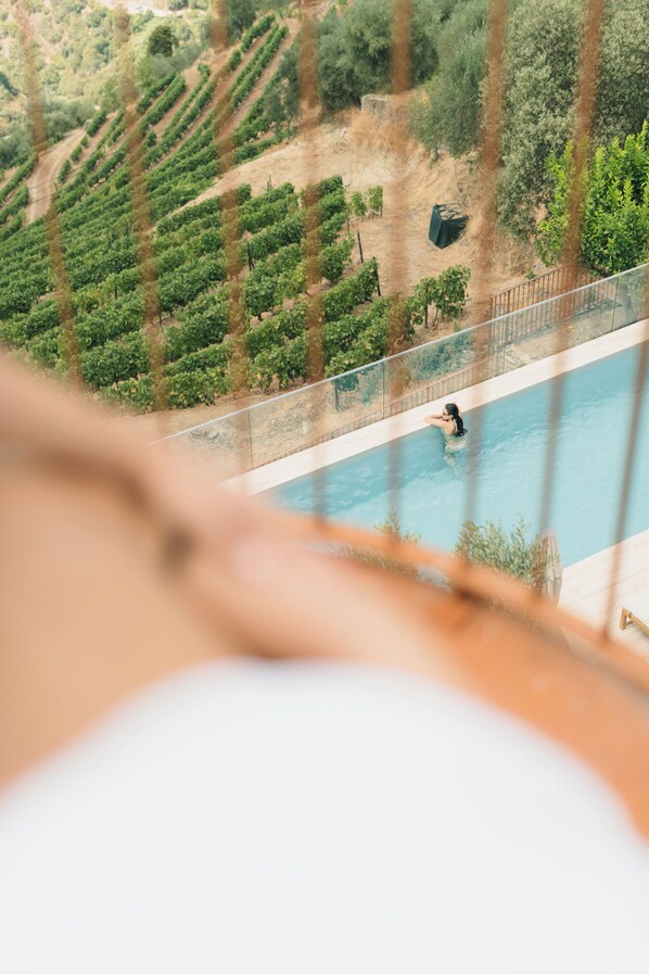 A pool with a person swimming, surrounded by a fence and a view of a vineyard.