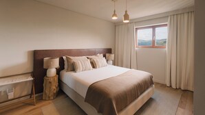 A bedroom with a large bed, two bedside lamps, a wooden nightstand, a window with curtains, and a view of the outdoors. - Douro Olive Hills Village - by FERO (Alijo)