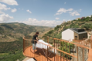 Un balcón con vistas a viñedos escalonados y un pueblo en la ladera.
