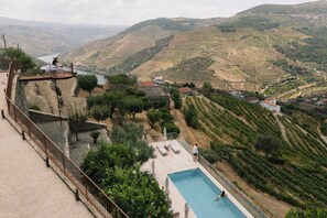 A pool with a view of terraced vineyards and a distant body of water.