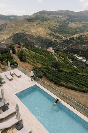 A swimming pool with lounge chairs and a view of terraced vineyards. - Douro Olive Hills Village - by FERO (Alijo)