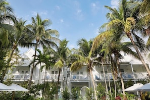 Ein Hotel direkt am Strand mit mehreren Balkonen, Palmen und blauem Himmel.
