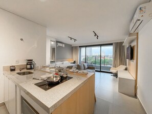 A modern hotel room with a kitchen area, a dining table, a sofa, and a balcony with a city view.