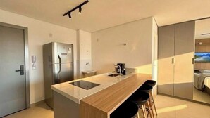 A modern kitchen with a central island, stainless steel appliances, and a view into a bedroom.