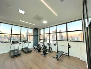 A gym with cardio equipment, weightlifting stations, and large windows with a city view.