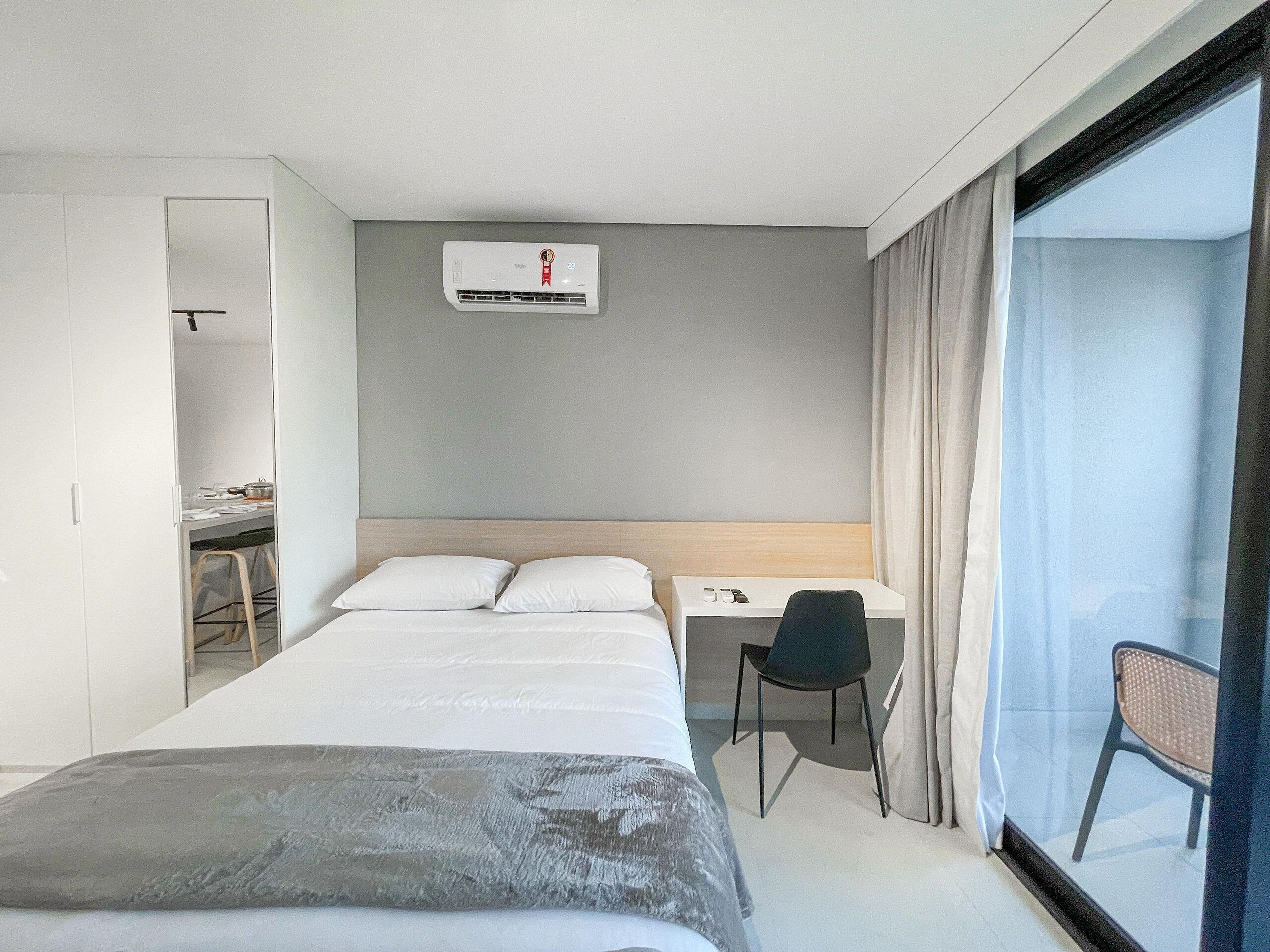 Habitación de hotel con cama, escritorio, silla y una ventana grande.
