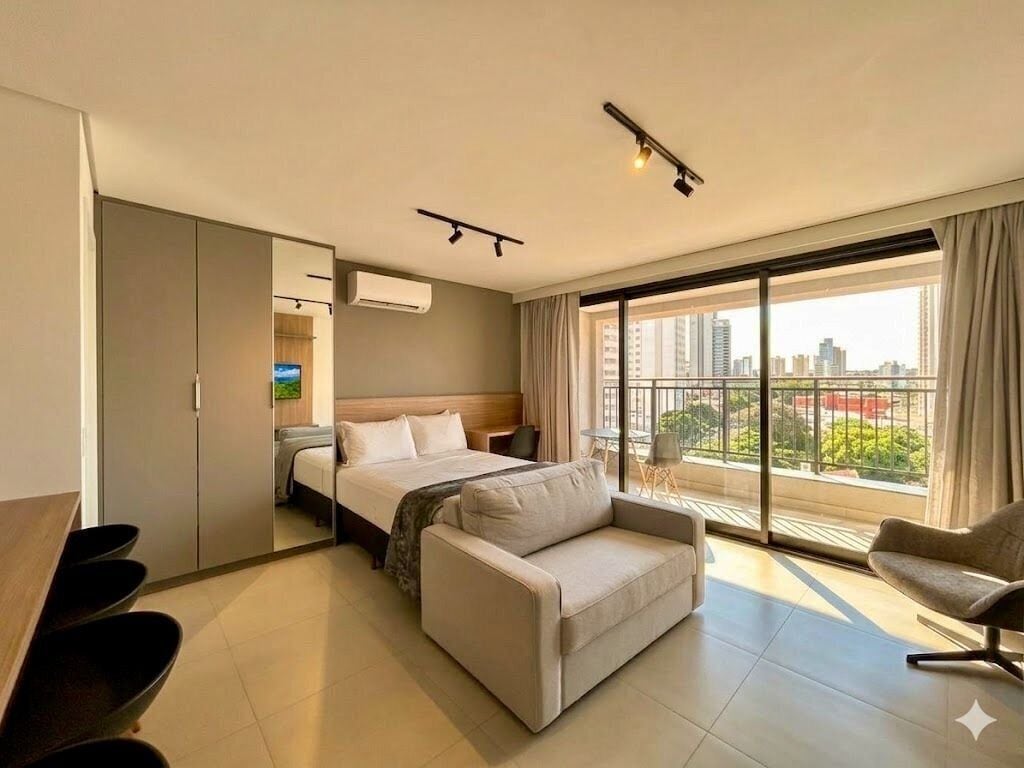 Quarto de hotel com cama, sofá, mesa de escritório e varanda com vista para a cidade.