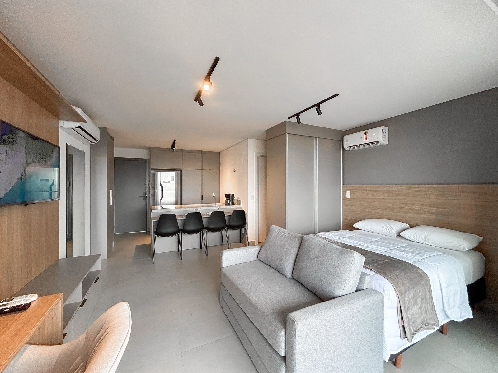 A modern hotel room with a sofa, a bed, a desk, and a kitchenette.
