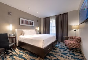 Ein Hotelzimmer mit einem großen Bett, einem Schreibtisch mit Stuhl, einem Fernseher und einem gemusterten Teppich.