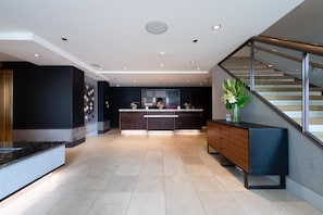Eine moderne Hotellobby mit einer Rezeption, einer Treppe und einer dekorativen Vase auf einem Konsolentisch.