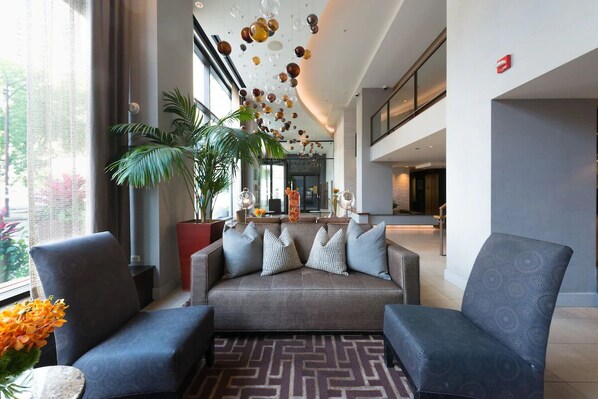 Eine moderne Lobby mit einer Couch, Sesseln, einem gemusterten Teppich und einer Decke mit hängenden Verzierungen.