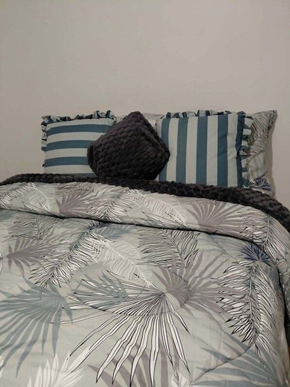 A bed with a patterned duvet, pillows with ruffled edges, and a dark textured throw.