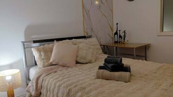 A bedroom with a bed, pillows, a bedside table with decorative items, a lamp, and a wall clock.