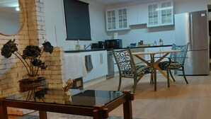 Una cocina moderna con armarios blancos, un refrigerador y un microondas. Hay un comedor con una mesa de vidrio y sillas.
