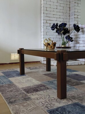 A wooden bench with a vase of flowers and a decorative item on it, placed on a patterned rug in a room with a white brick wall.
