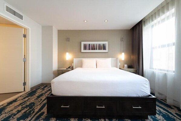 Ein Hotelzimmer mit einem großen Bett, Nachttischen, einem Wandbild und einem Fenster mit Vorhängen.