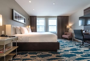 Ein Hotelzimmer mit Bett, Schreibtisch, Stuhl und großen Fenstern.