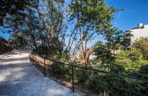A pathway with a metal railing, surrounded by trees and greenery, leading to a building. - Casa Mirador Luxury 3 bedroom Condo, Panoramic Ocean Views (Puerto Vallarta)