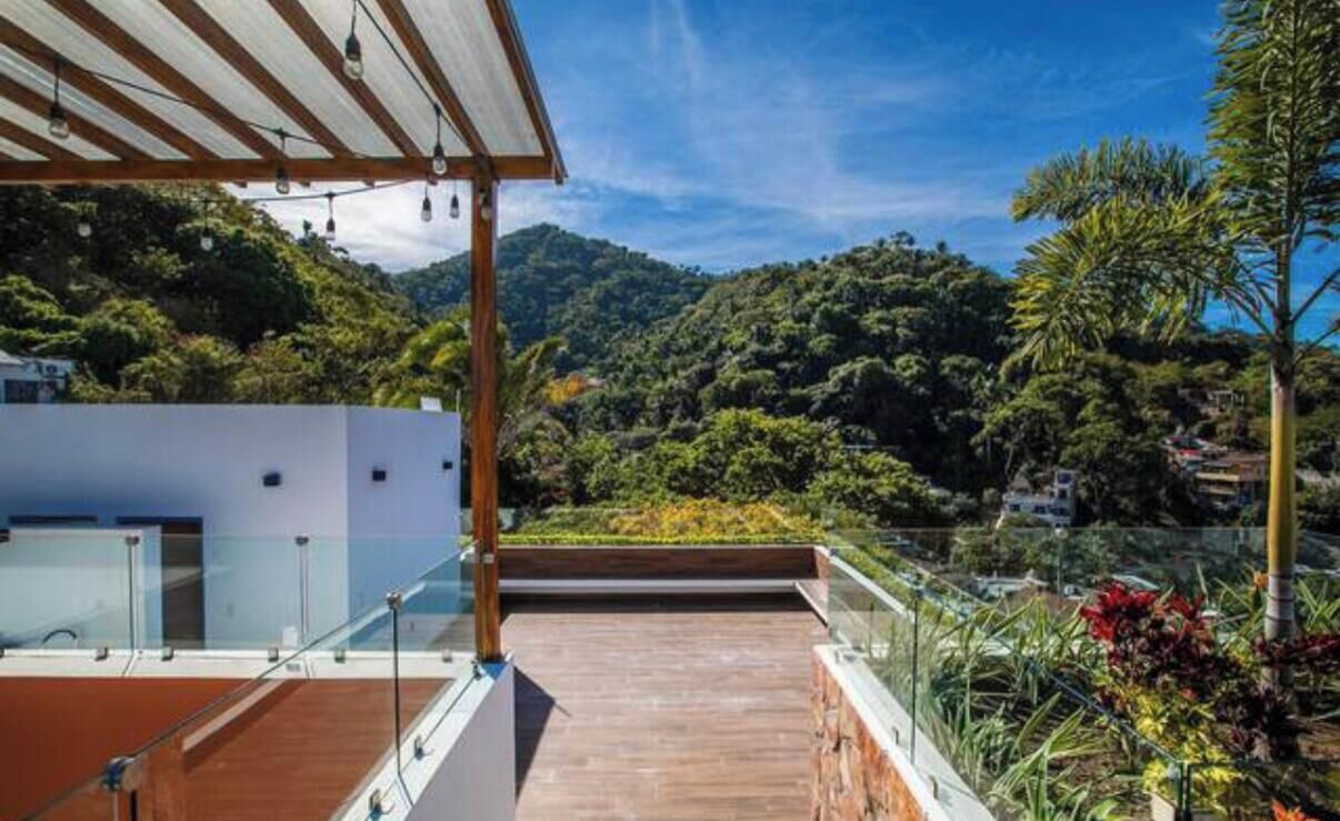 Eine Dachterrasse mit Holzdeck, Glasgeländern und Blick auf eine Berglandschaft.