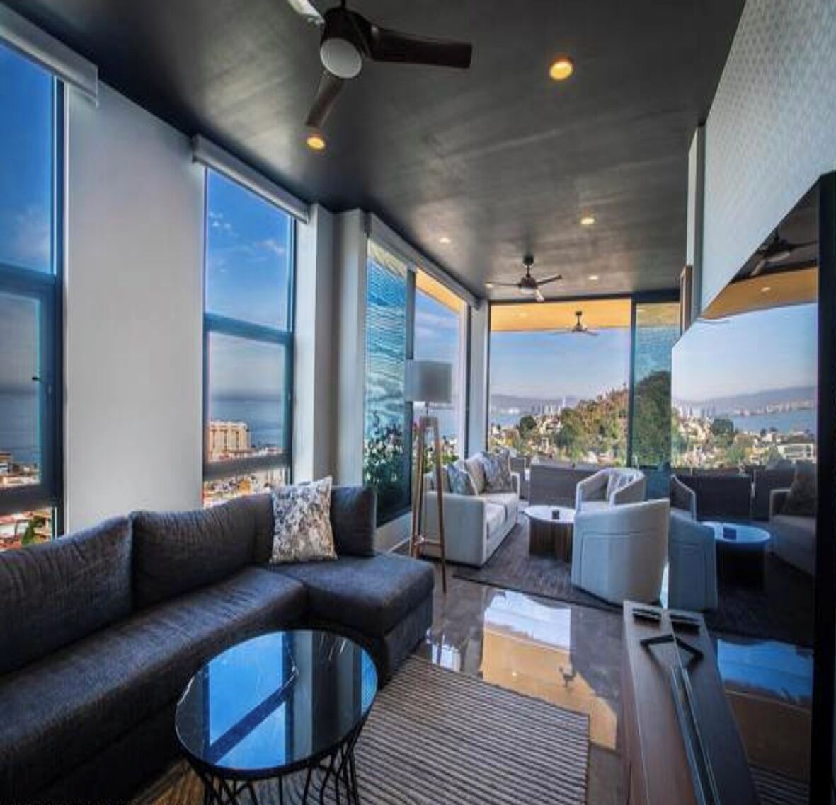Ein stilvolles Wohnzimmer mit Sofa, Sesseln und Couchtisch, mit großen Fenstern und Blick auf die Stadt.