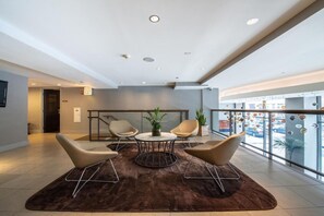 Een moderne lobby met een zithoek, een ronde tafel en uitzicht op het buitenlands gebied door grote ramen.