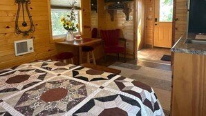 A cozy cabin interior with a wooden ceiling, a quilted bedspread, a dining area with a table and chairs, a television, and a kitchen area. - Byrd Homestead - Hill Top (Carmen)
