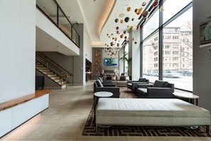 Een moderne lobby met een trap, een zithoek en grote ramen met uitzicht over de stad.