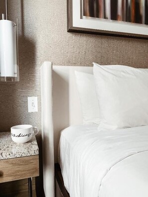 Ein Hotelzimmer mit einem Bett, einem Nachttisch, einem gerahmten Bild und einer Kaffeetasse.