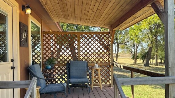 Una terraza de madera con techo rojo, dos sillas, una mesita y un celosíería.