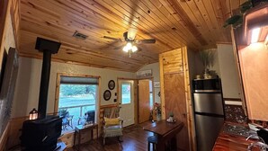 Interior acogedor de una cabaña con techo de madera, una zona de comedor, una cocina con refrigerador y una chimenea.