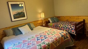 Una habitación con dos camas, cada una con una colcha, una mesita de noche con una lámpara y un cuadro en la pared.