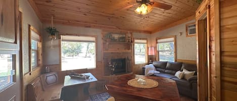 Interior de madera con comedor, sofá, chimenea y ventilador de techo.