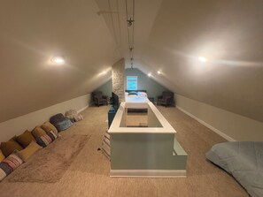 Une pièce avec un plafond en pente, un lit, un téléviseur et un coin salon avec des coussins.