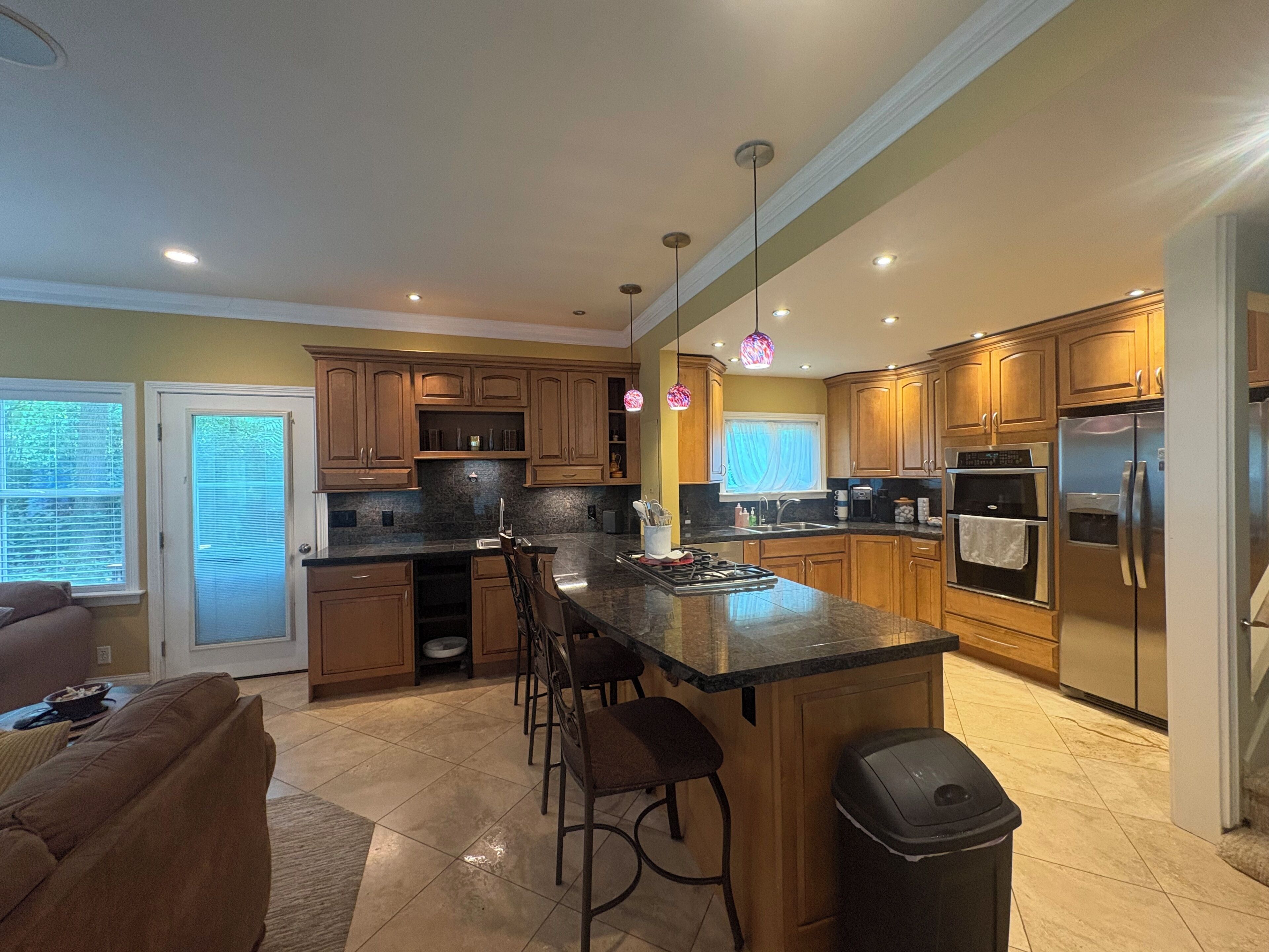 A kitchen with wooden cabinets, a granite countertop, a stainless steel refrigerator, and a built-in oven.