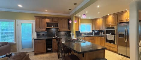 A kitchen with wooden cabinets, a granite countertop, a stainless steel refrigerator, and a built-in oven.
