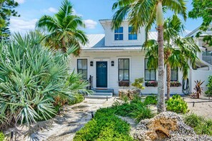 A white house with a blue door, surrounded by tropical plants and a well-maintained garden. - 4 King Beds + Guest House • Heated Pool/Spa (Anna Maria)