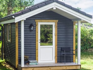 A small wooden cabin with a white door, a porch with a chair, and a lantern on the wall.